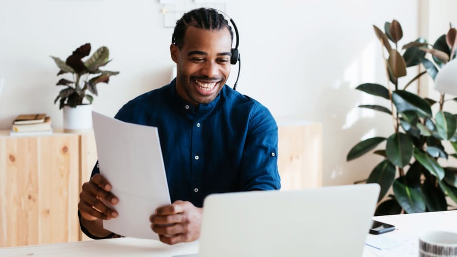 Hombre con auriculares mirando la pantalla del portátil sosteniendo papel - ventas remotas de smb