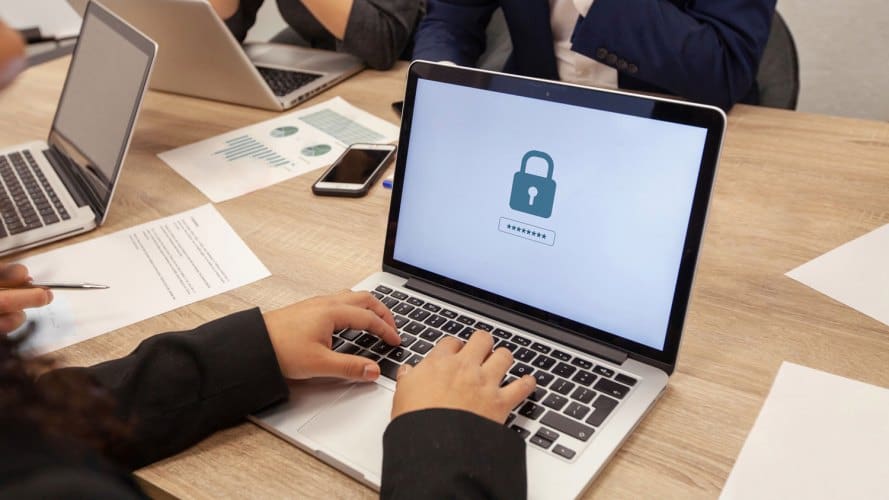 computadoras portátiles en una mesa con las manos, la pantalla de la computadora portátil tiene una imagen de un candado que indica cómo evitar ataques de ciberseguridad