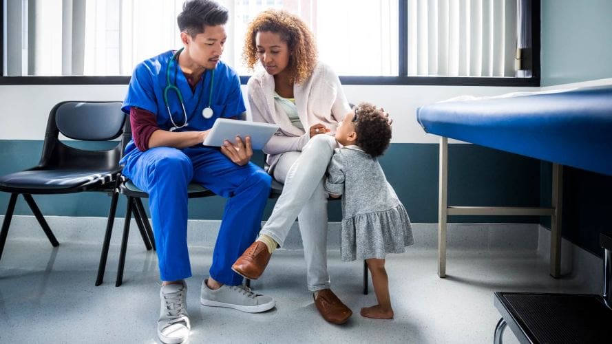 profesional de la salud masculino sentado con una madre y un niño mirando archivos